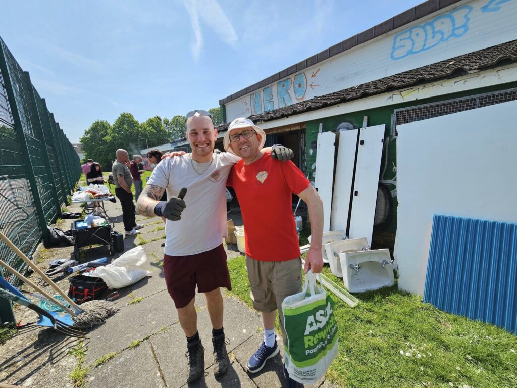 Coach Joel and a volunteer smiling for a photo during a community action day.